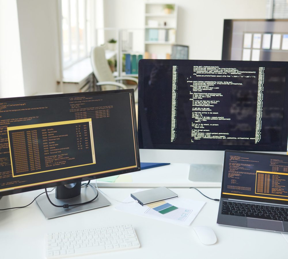 Background image of several computer screens with code lines on desk in IT developers office, copy space